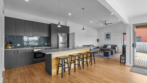 A modern kitchen with a central island, bar stools, and a dining area with a sofa and coffee machine. - Igneous Ridge - Calm and Quiet Retreat (Port Fairy)