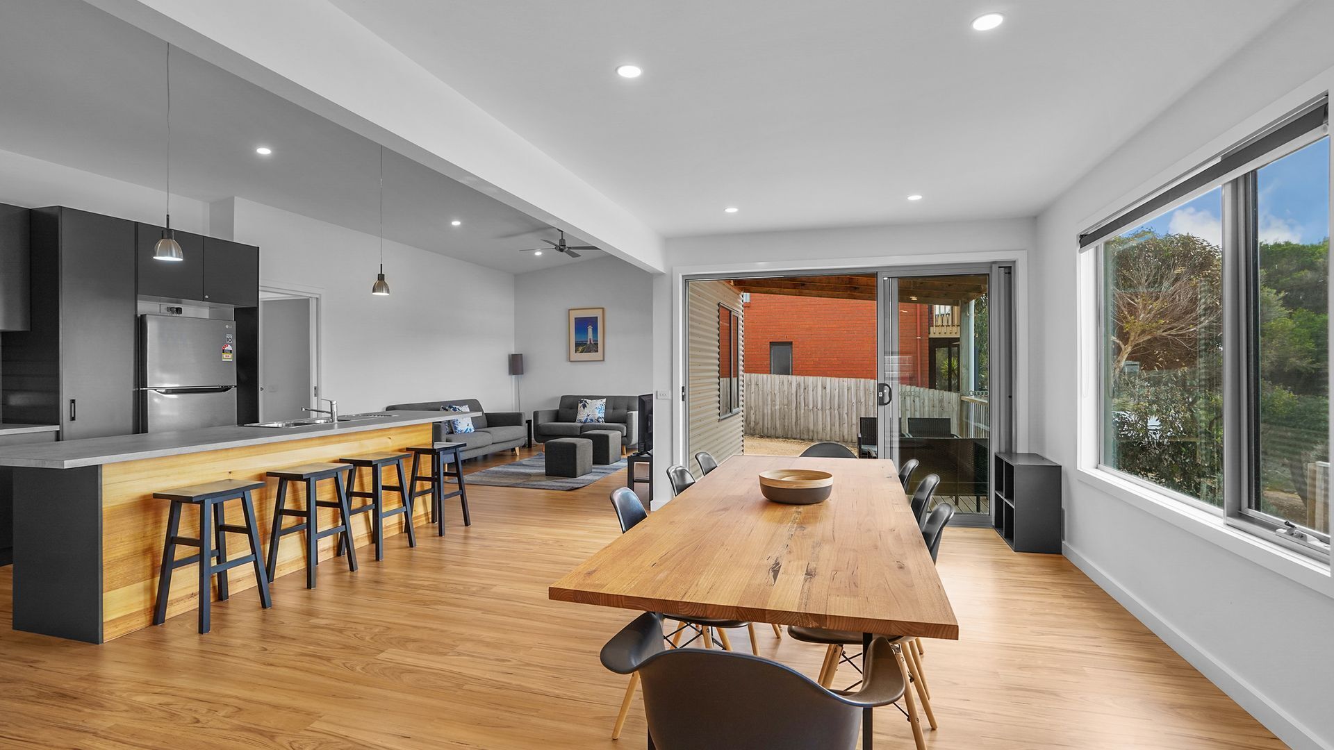 Une cuisine moderne dotée d’un îlot central, de tabourets de bar et d’un coin repas avec une table et des chaises en bois.