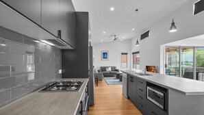 A modern kitchen with grey cabinets, a stainless steel stove, and a large window offering a view of the outdoors. - Igneous Ridge - Calm and Quiet Retreat (Port Fairy)