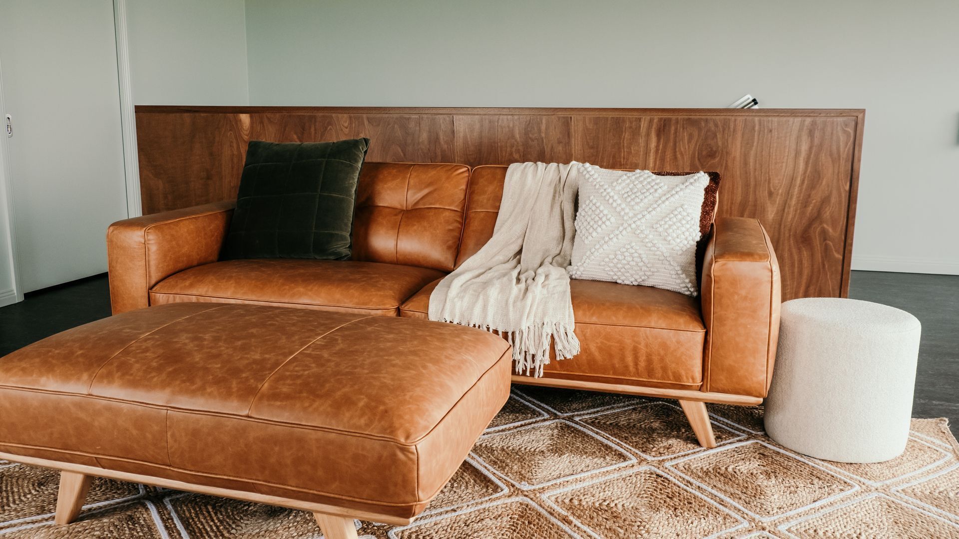 Un canapé en cuir marron assorti d’un pouf, une tête de lit en bois et un tapis à motifs.
