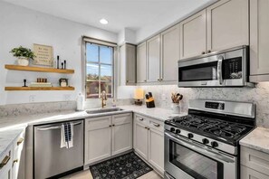 Una cocina moderna con armarios grises, una estufa de acero inoxidable, un microondas y un ventanal que proporciona luz natural.