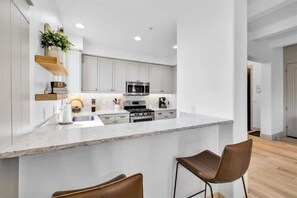 Une cuisine moderne avec des meubles blancs, un îlot central doté de tabourets de bar et un four à micro-ondes placé au-dessus de la cuisinière.