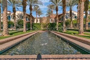 A pool with a fountain, surrounded by palm trees and buildings.