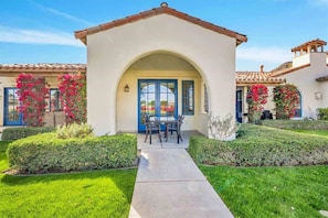 A house with a white exterior, a blue door, and a patio with a table and chairs. - Modern Palms B | Studio Legacy Villa (La Quinta)