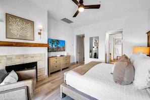 A modern bedroom with a large bed, a fireplace, a ceiling fan, and a painting on the wall. - Modern Palms B | Studio Legacy Villa (La Quinta)