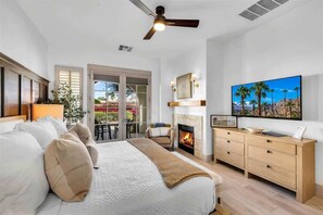 A bedroom with a bed, a fireplace, a television, and a balcony with a view. - Modern Palms B | Studio Legacy Villa (La Quinta)
