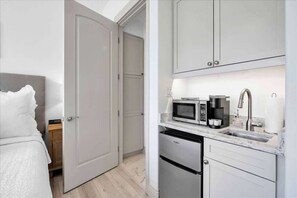 A compact hotel room with a bed, a small kitchenette with a microwave, coffee maker, and sink, and a wardrobe.