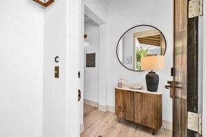 Een hal met een houten kast, een ronde spiegel en een deur met een 'C'-bordje.
