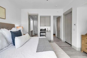 Een moderne hotelkamer met een groot bed, nachtkastje, lamp en uitzicht op de keuken.