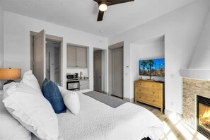 Un dormitorio con cama, televisor, chimenea y una zona de cocina visible a través de una puerta abierta.
