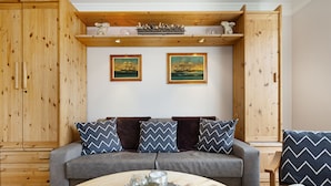 Een gezellige woonkamer met een grijze bank, houten wanden en twee ingelijste schilderijen.