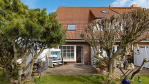 Een huis met pannendak, terras met buitenmeubilair en een tuin met diverse planten en decoraties.
