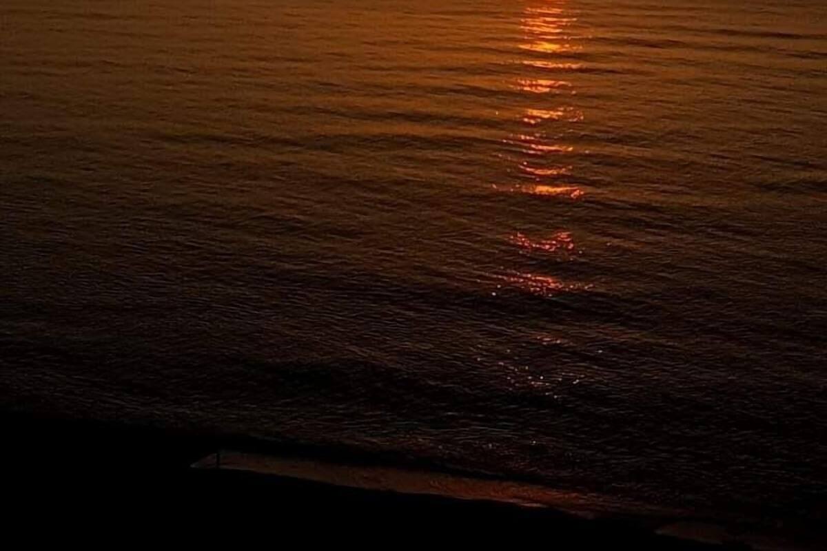A sunset over a calm sea with a distant mountain.