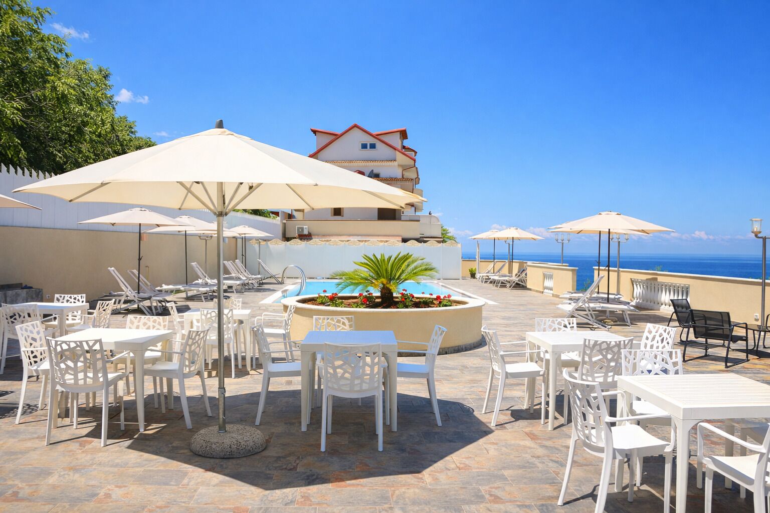 An outdoor patio with white tables and chairs, umbrellas, and a pool area.