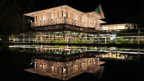 Un edificio de varios pisos con una superficie acuática reflectante en primer plano, que presenta un estilo arquitectónico tradicional y una bandera verde en la parte superior.