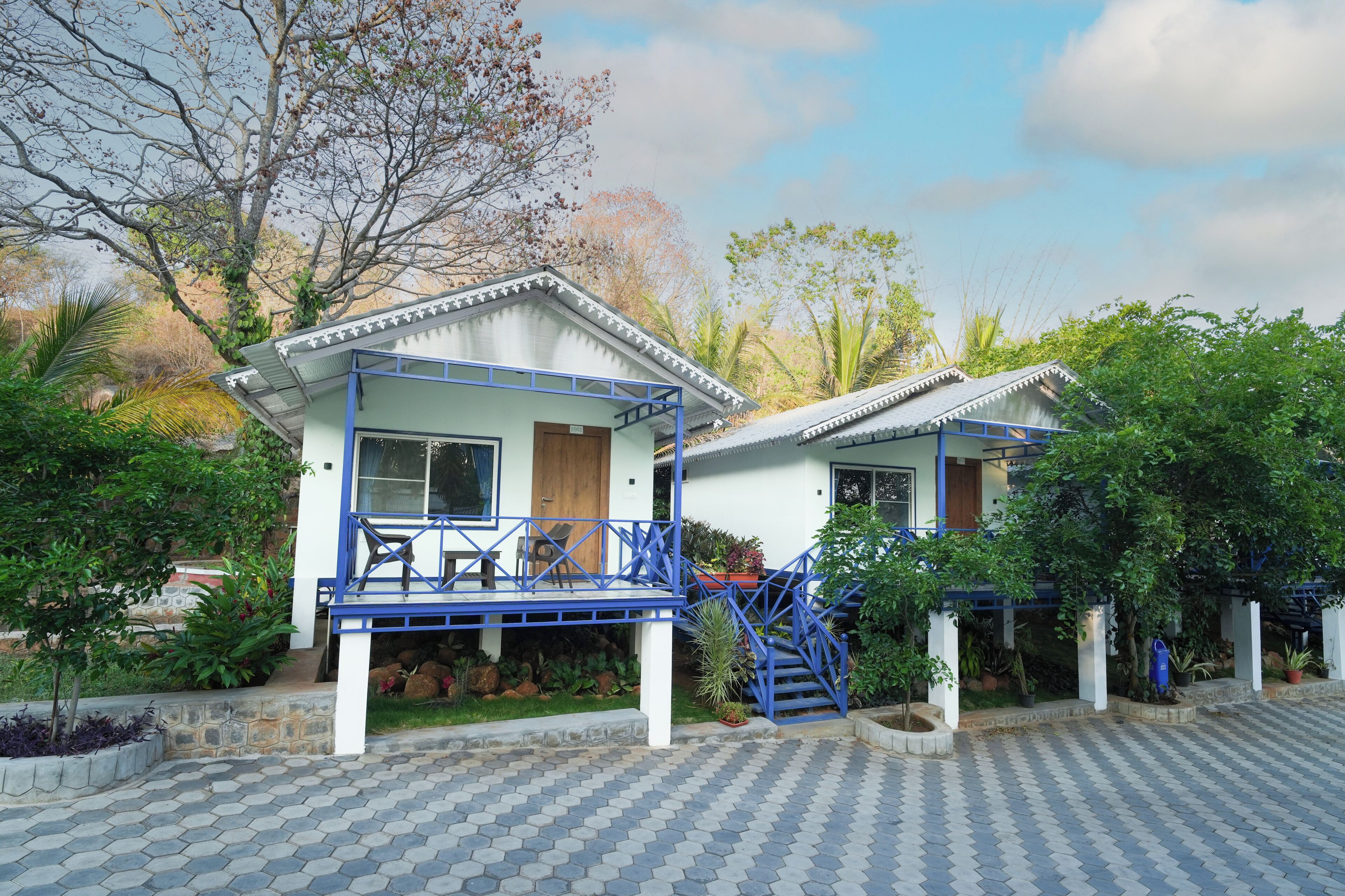 A bungalow-style hotel with a blue and white color scheme, a covered outdoor seating area, and a staircase leading to the entrance.