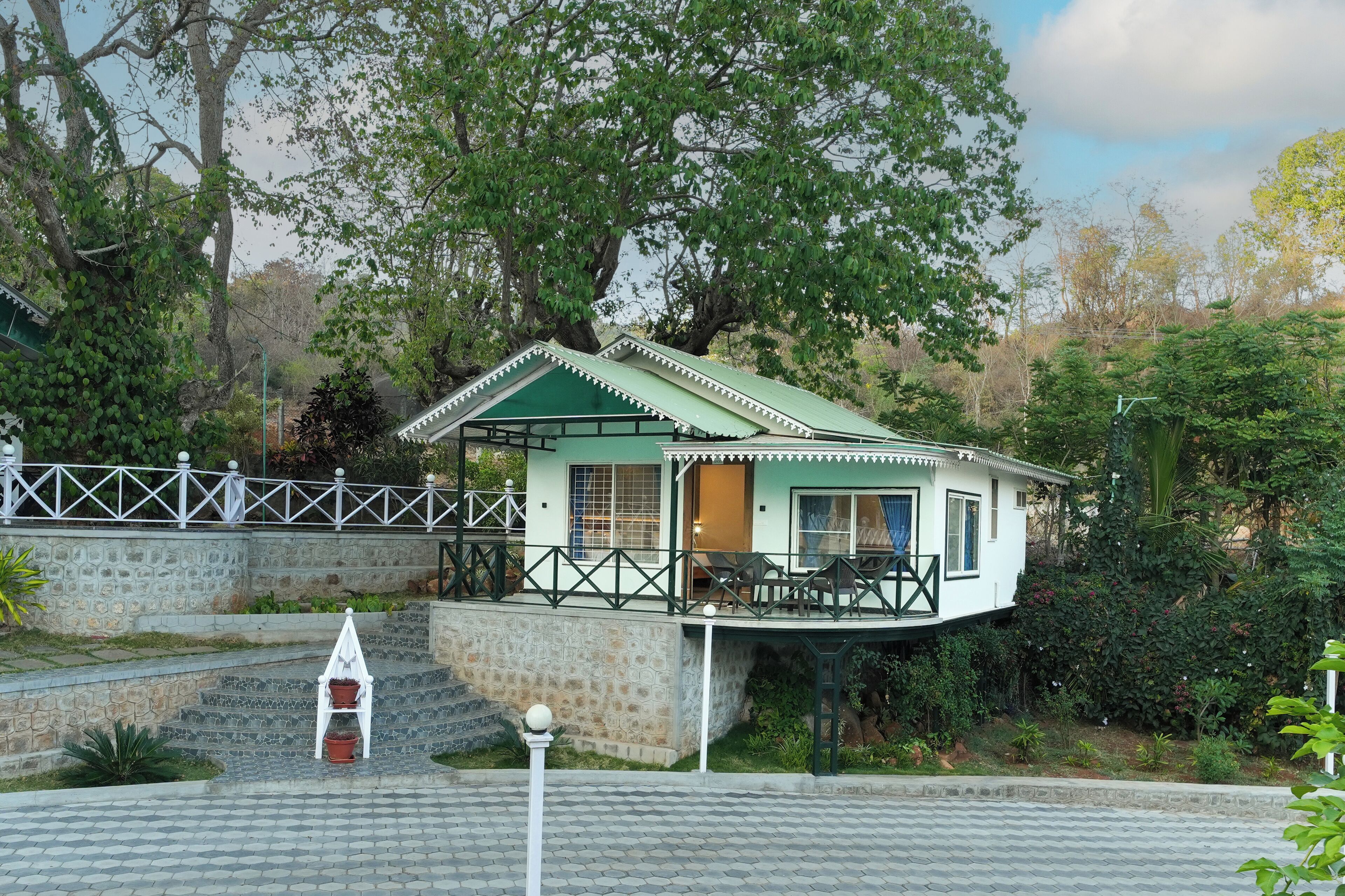A house with a balcony, surrounded by trees and a stone wall.