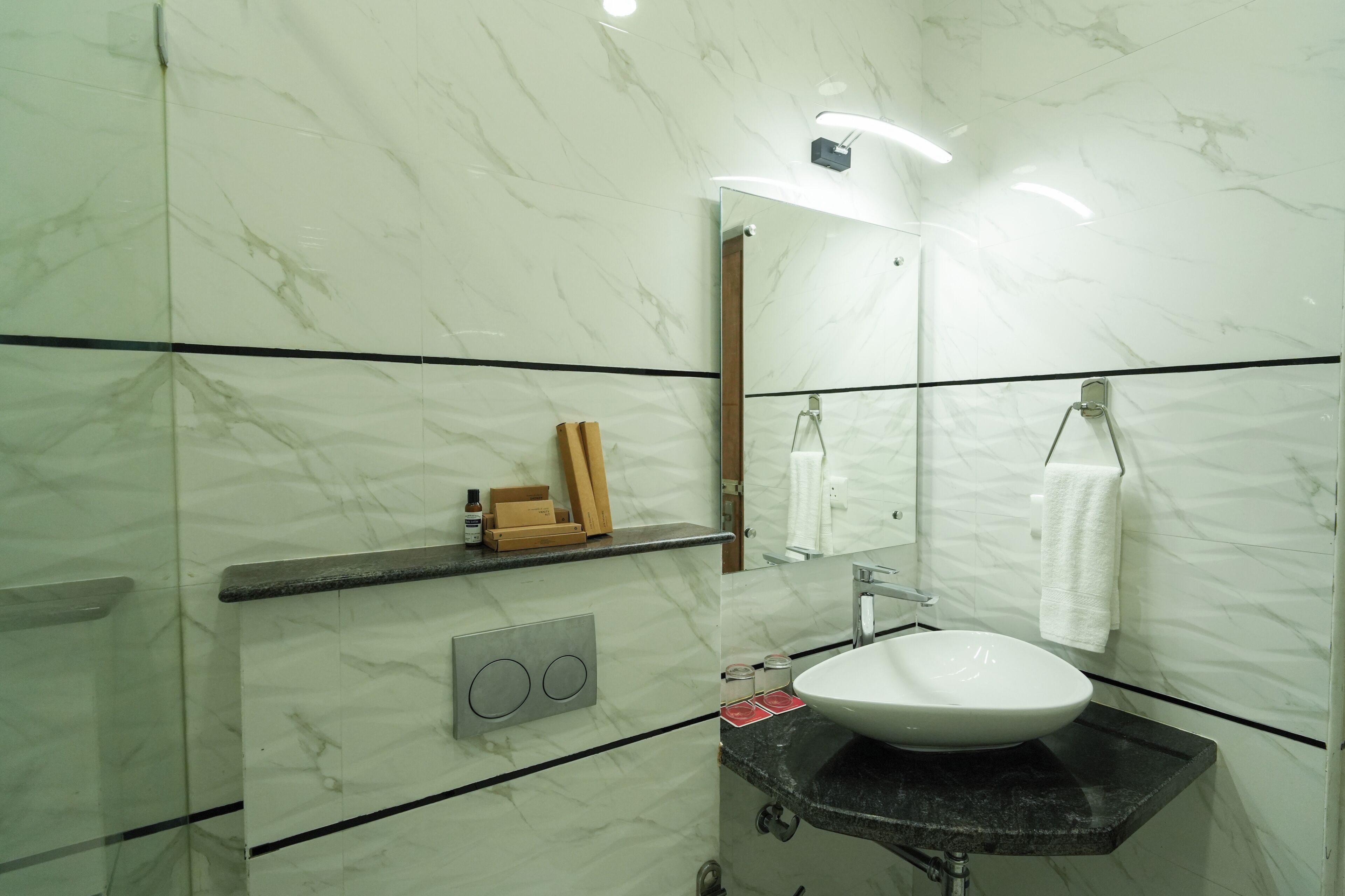 Un baño con pared de mármol, un lavamanos, un espejo y un perchero para toallas.