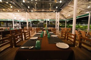Ein Restaurant mit überdachter Außenbereich, Holztischen und -stühlen und Blick auf Grünflächen.