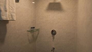 A small, enclosed shower area with a glass door, a towel rack, and a shelf with toiletries.