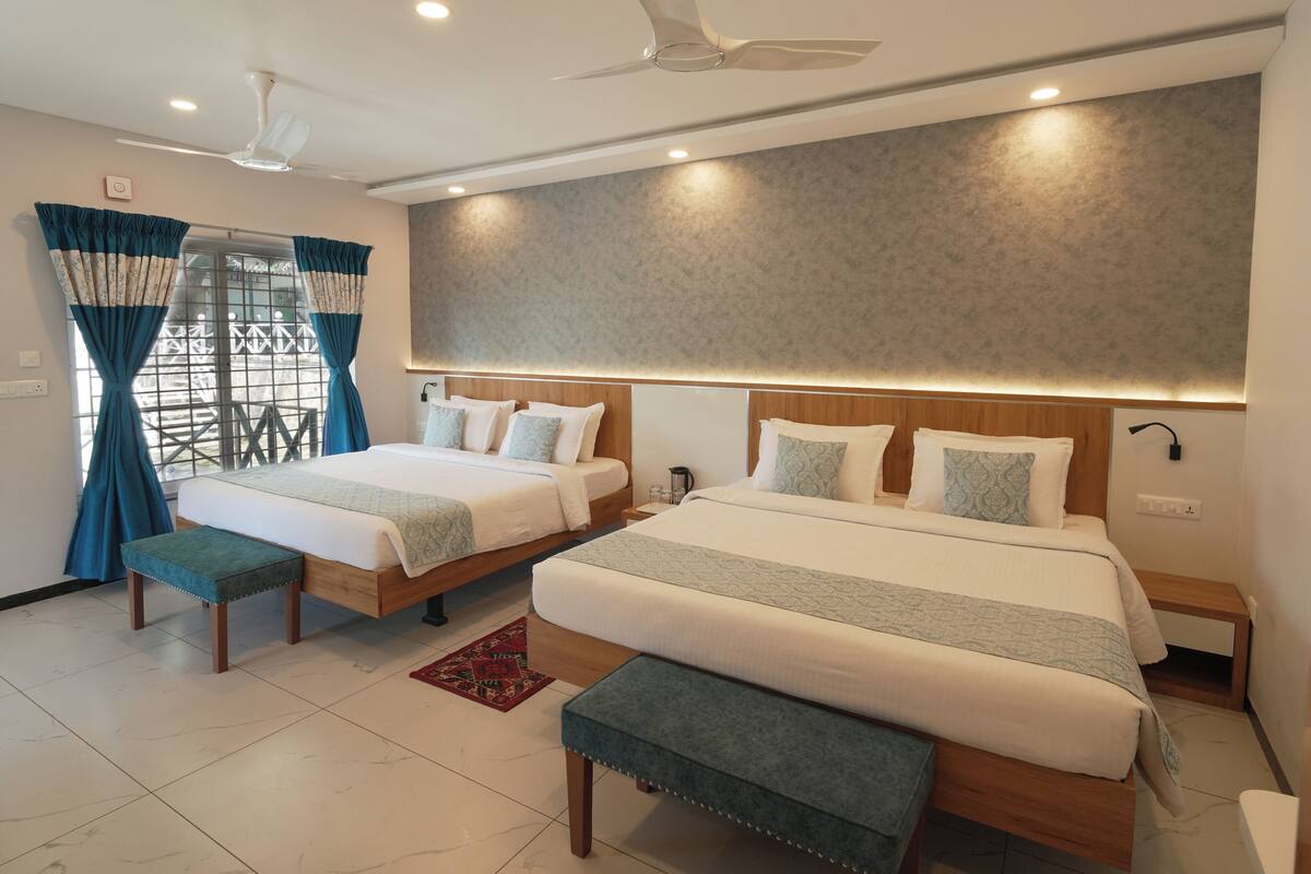 Habitación de hotel con dos camas, ventilador de techo y un ventanal con cortinas.