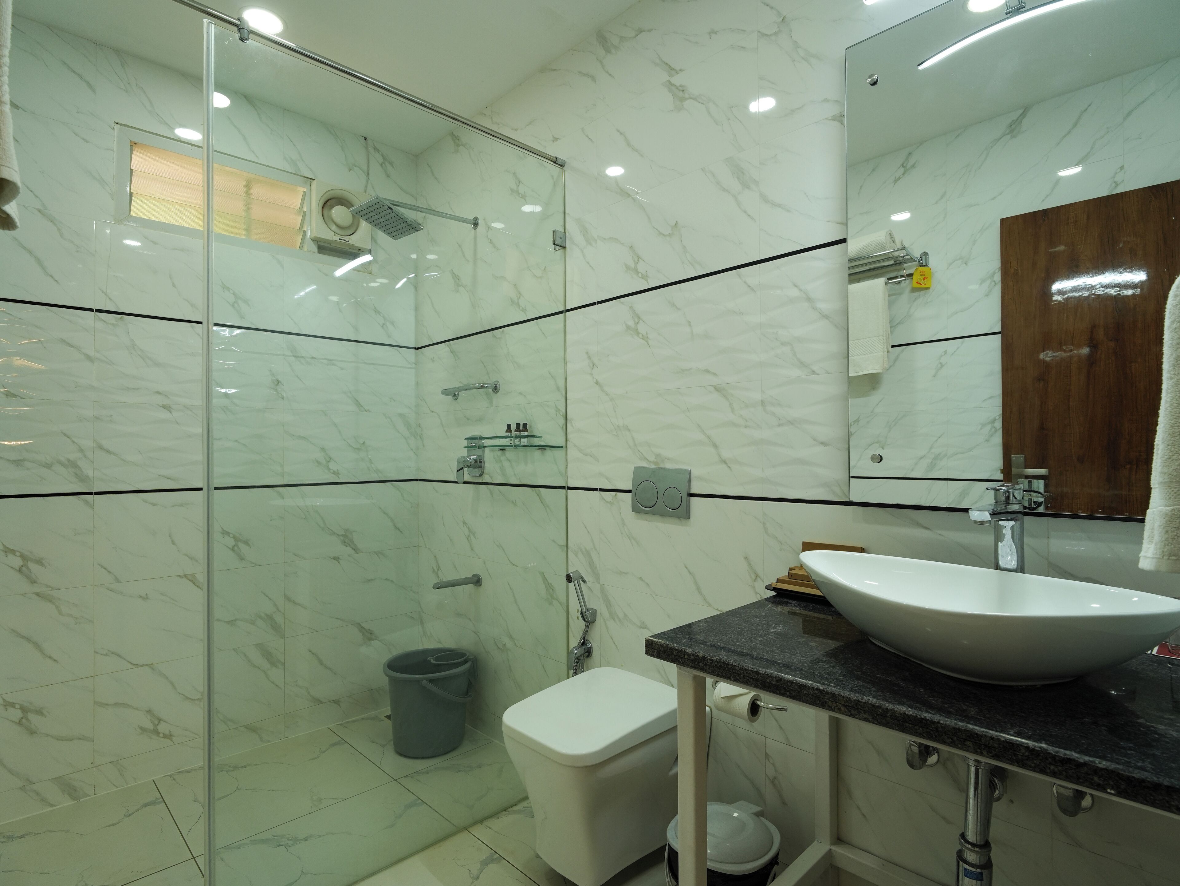A modern bathroom with a glass-enclosed shower, a white toilet, a sink with a marble countertop, and a mirror above the sink.