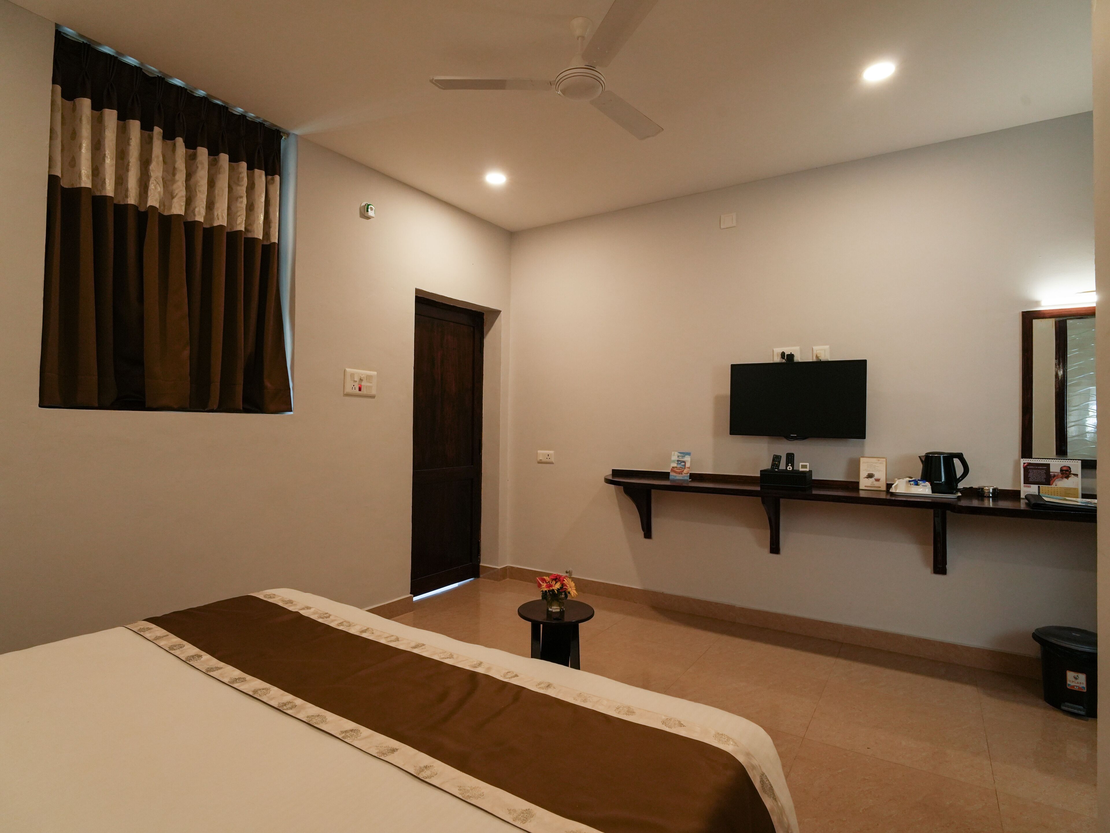 A hotel room with a bed, a TV, a small table with a remote control, a mirror, and a ceiling fan.