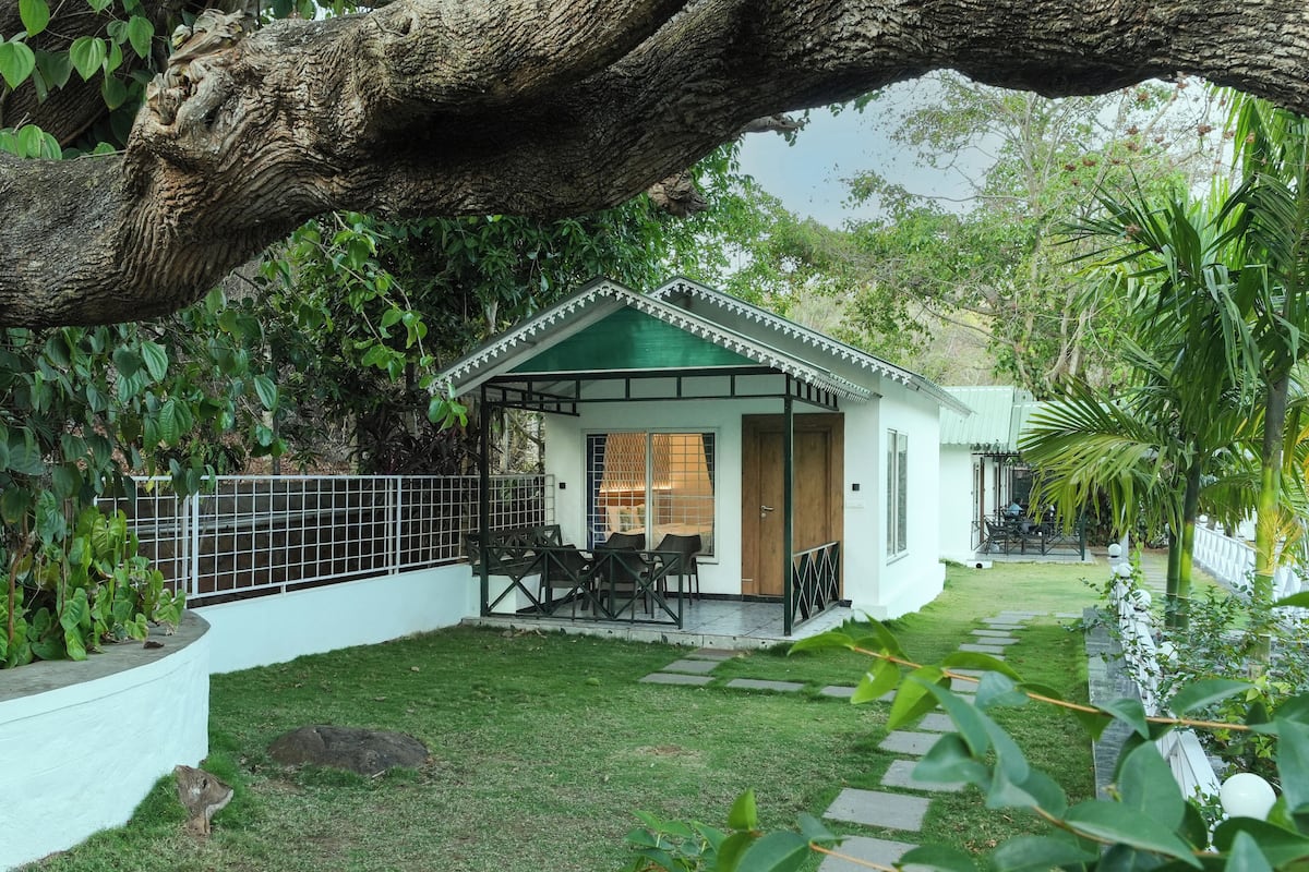 Una casita con techo verde, un patio con sillas y un jardín con sendero de piedra.