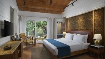 A hotel room with a bed, a television, a desk with a lamp, a chair, and a view of the outdoors.