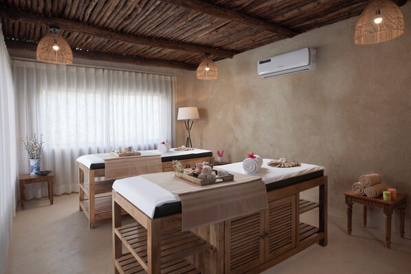 A spa room with wooden massage tables, a large window with sheer curtains, a floor lamp, and an air conditioning unit on the wall. - LaRiSa Resort & Spa, Ashwem (Ashvem)