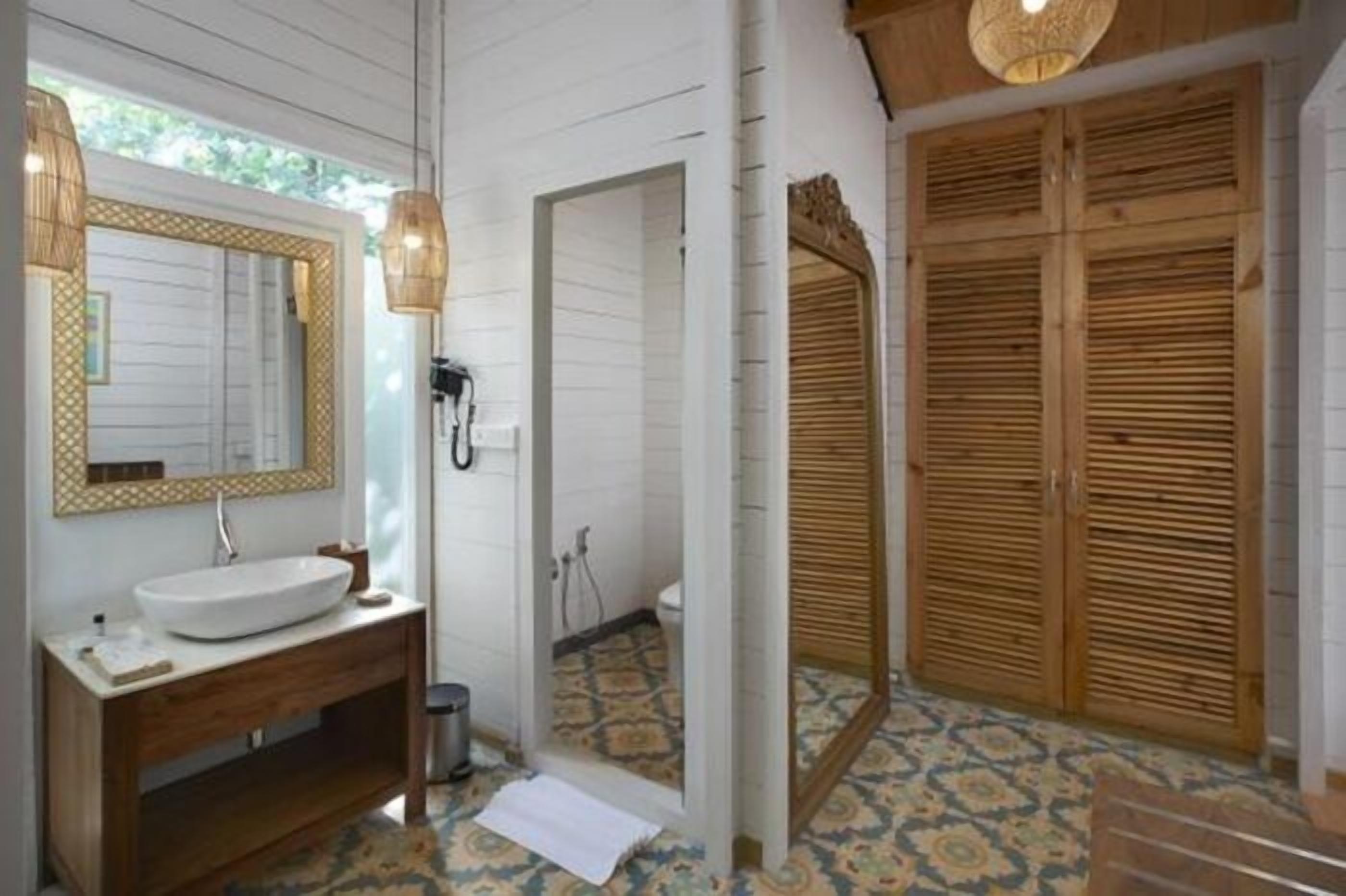 A bathroom with a wooden vanity, a large mirror, and a patterned floor.