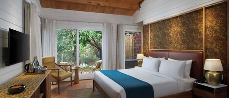 Habitación de hotel con techo de madera, una cama grande con ropa de cama blanca y un detalle en azul, un televisor de pantalla plana, un escritorio con un cuenco de fruta y vistas a zonas verdes.