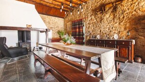 Ein rustikales Interieur mit einer Steinwand, Holzbalkendecke und einer Essecke mit Bänken und einem Tisch.