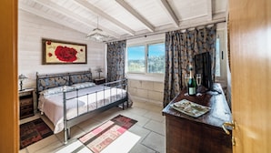 A bedroom with a metal bed frame, a wooden dresser, a nightstand, a window with curtains, and a painting of a rose on the wall. - Villa Civico 32 Near The Sea With Pool (Carpignano Salentino)