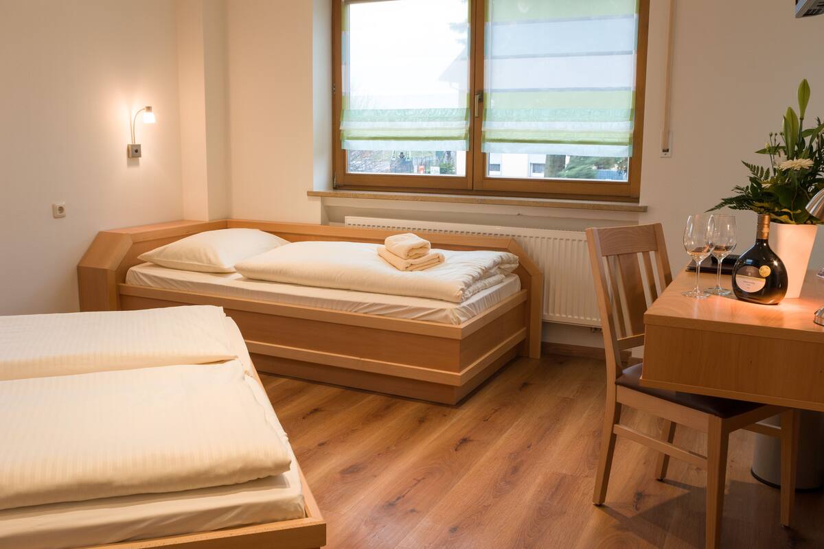 Un dormitorio con una cama de madera, una mesita con una botella y vasos, y una ventana con vistas.