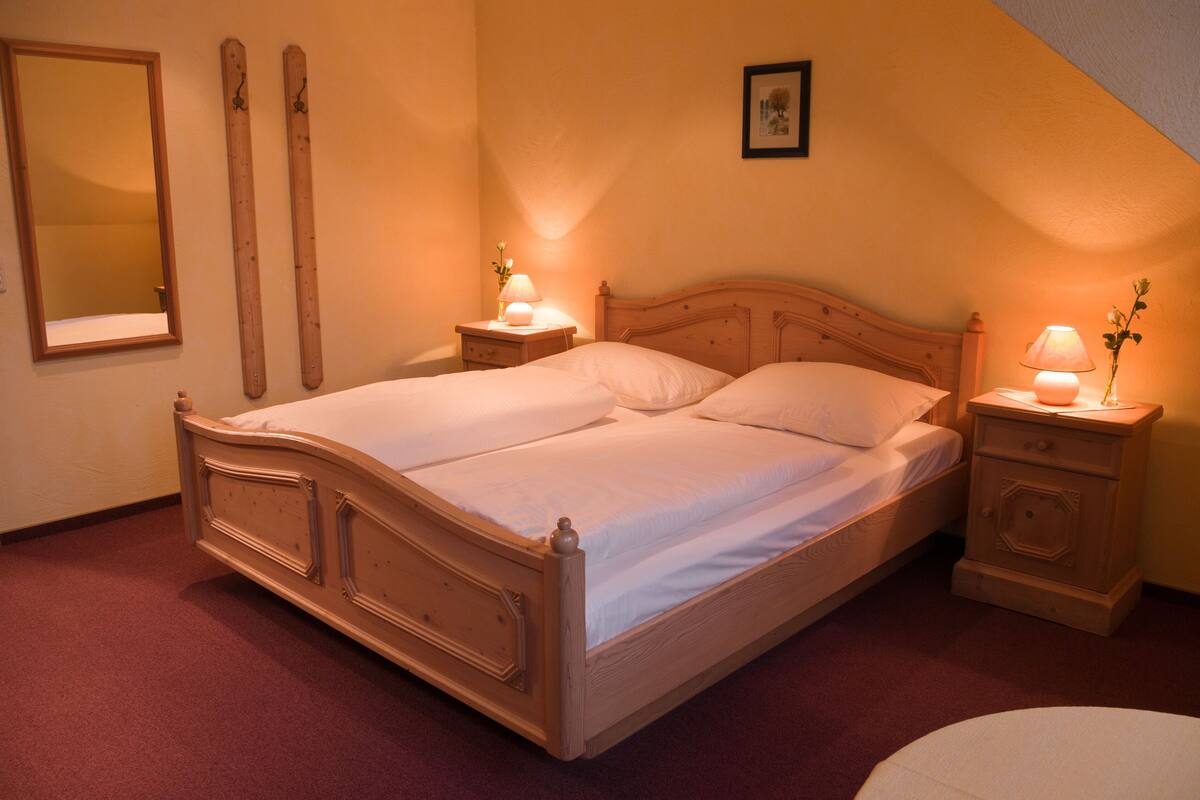 Un dormitorio con cama de madera, dos mesitas de noche con lámparas, un espejo y un cuadro en la pared.