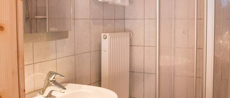 A bathroom with a sink, mirror, shower, and tiled walls.
