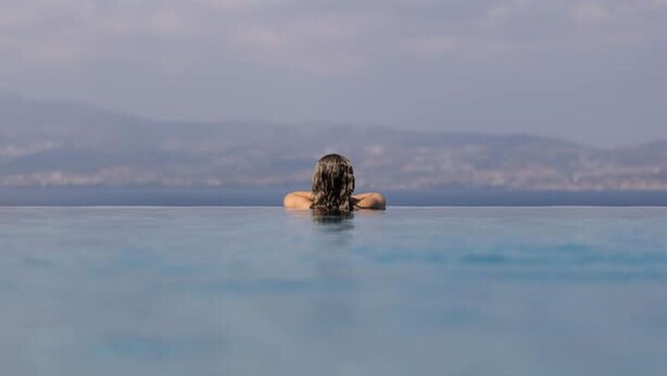 A person relaxing in a clear blue infinity pool with a mountainous backdrop. - Elanora Villa (Stelida)