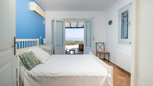 A bedroom with a bed, a chair, a table, and a view of the beach. - Elanora Villa (Stelida)
