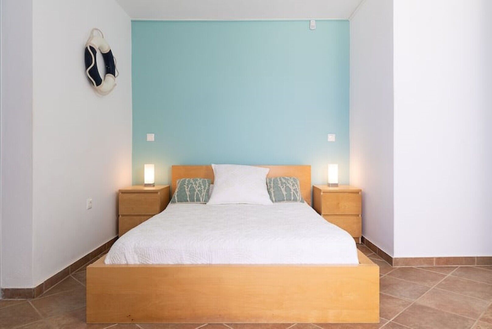 A bed with a wooden frame, two bedside tables with lamps, and a light blue wall.