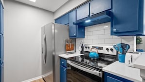 Eine Küche mit blauen Schränken, einem Edelstahl-Kühlschrank, einem schwarzen Herd und einem blauen Wasserkocher.