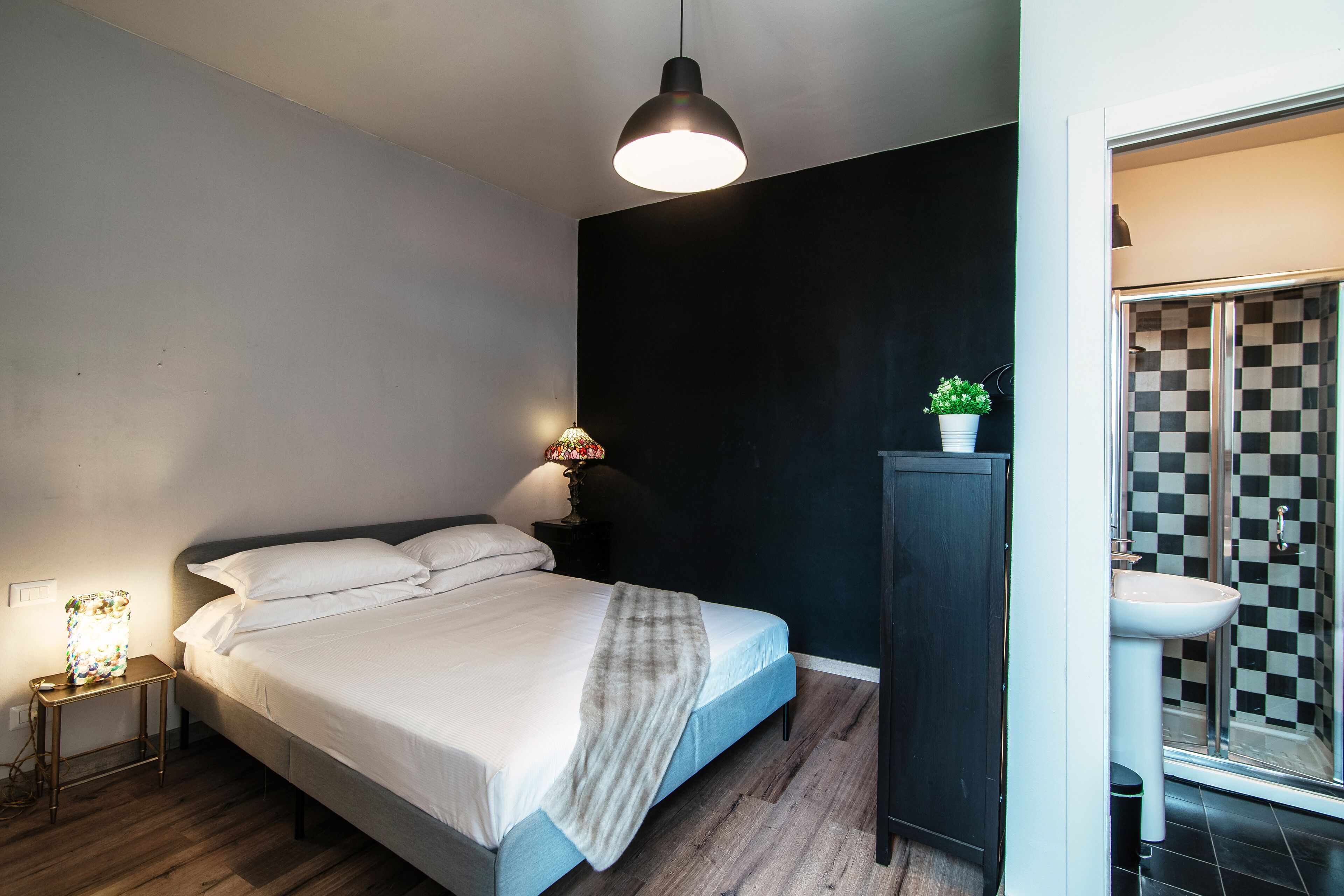 A bedroom with a bed, bedside lamp, and a small table with a lamp.