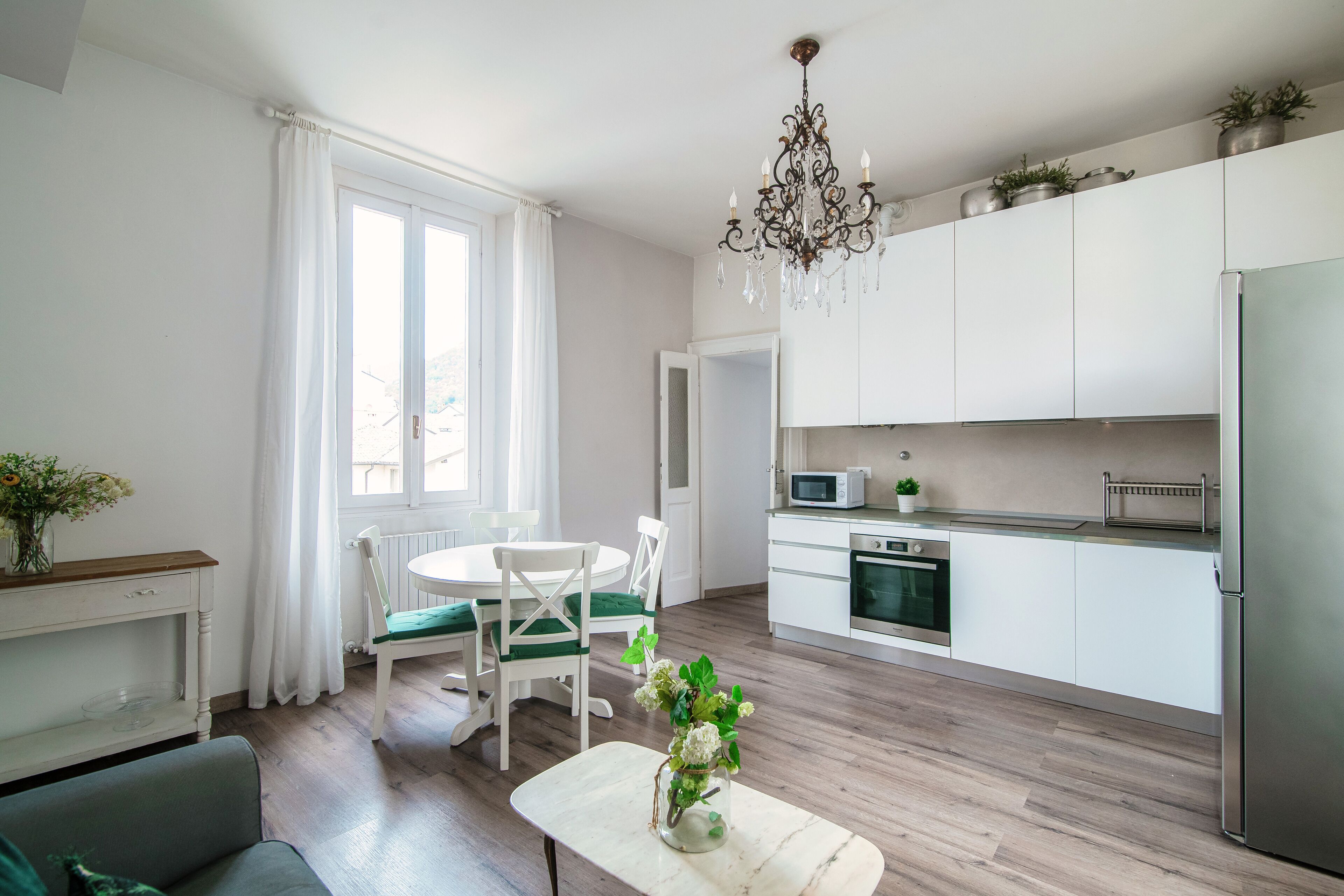 A modern kitchen with white cabinets, a dining area with a white table and chairs, and a chandelier.