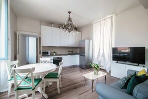 A modern kitchen with white cabinets, a stainless steel refrigerator, and a flat-screen TV. - Glamour (Como)