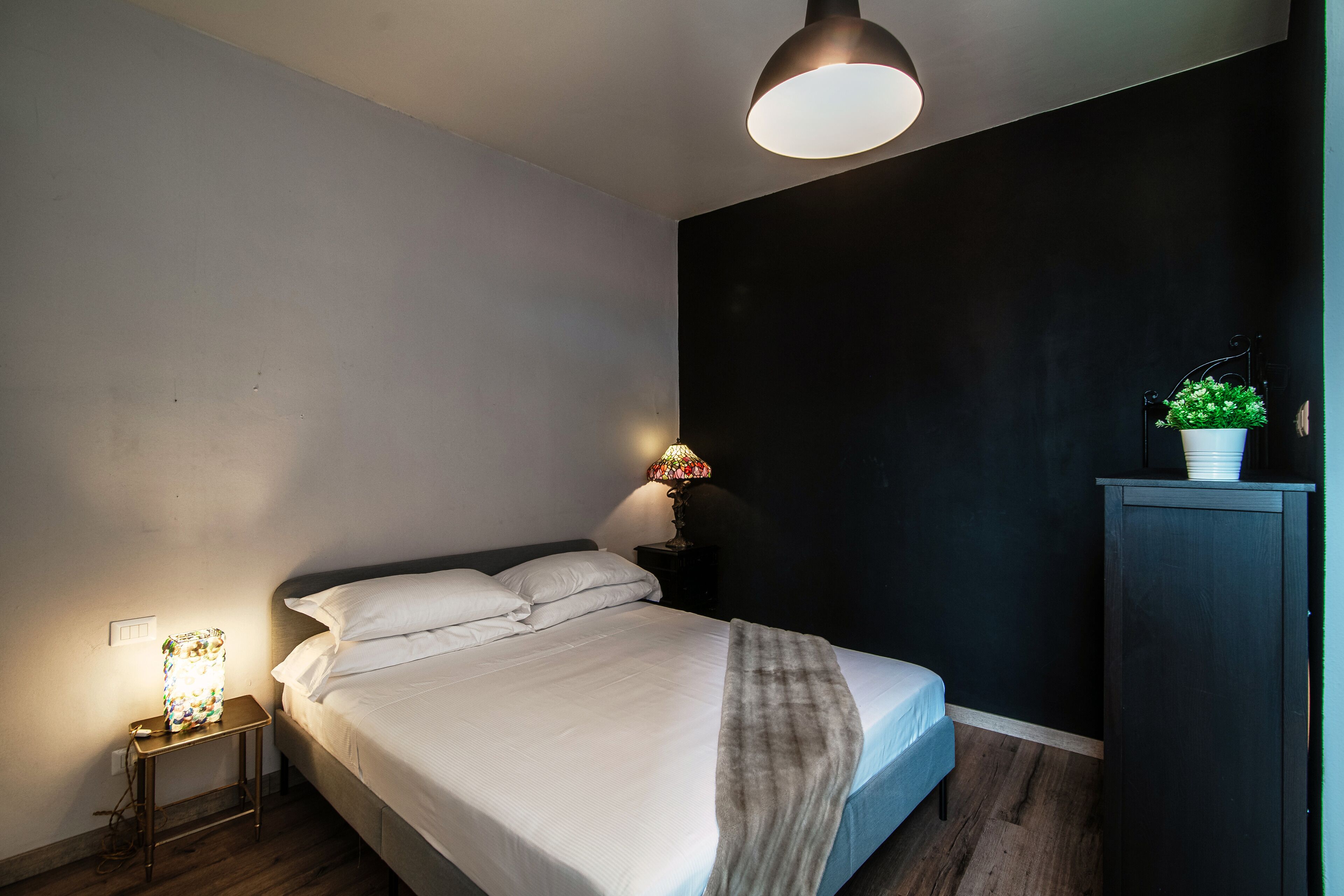 A bedroom with a bed, bedside lamp, and a small table with a lamp.