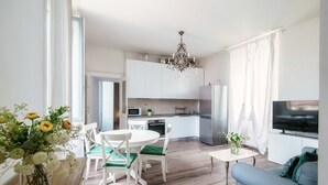 A modern kitchen with white cabinets, a chandelier, and a dining area with white chairs and a table. - Glamour (Como)