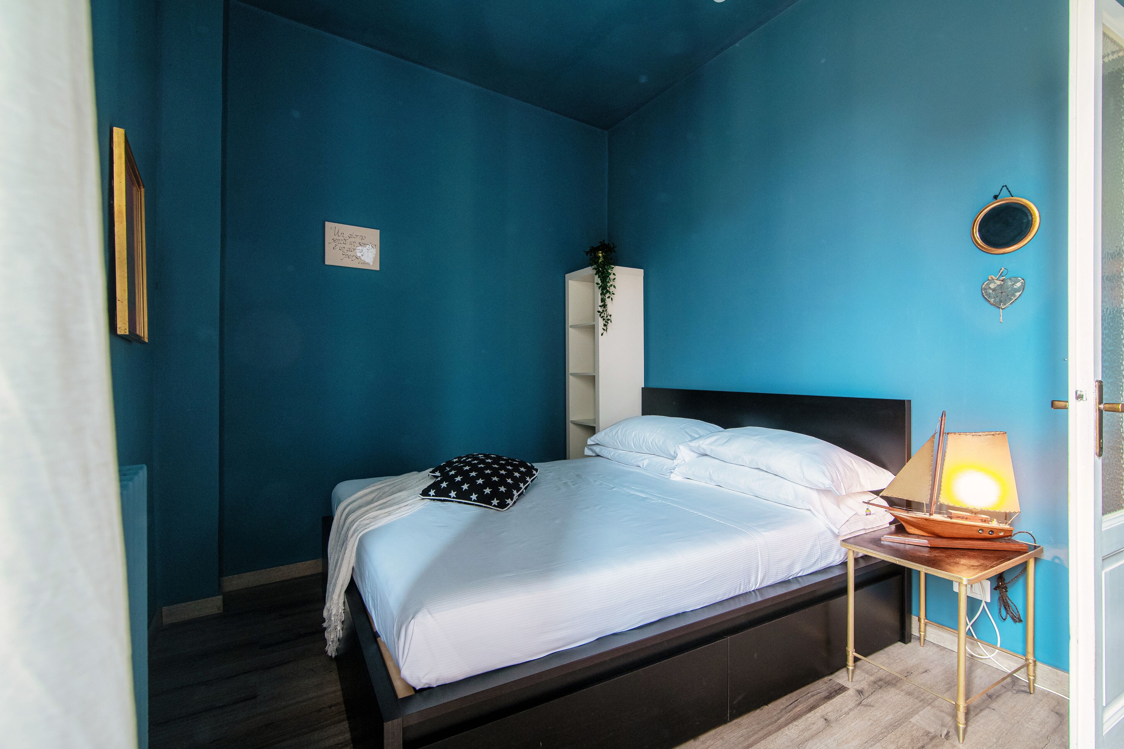 Ein Schlafzimmer mit einem Bett, einem Nachttisch, einer Lampe, einem Spiegel und einer Pflanze.