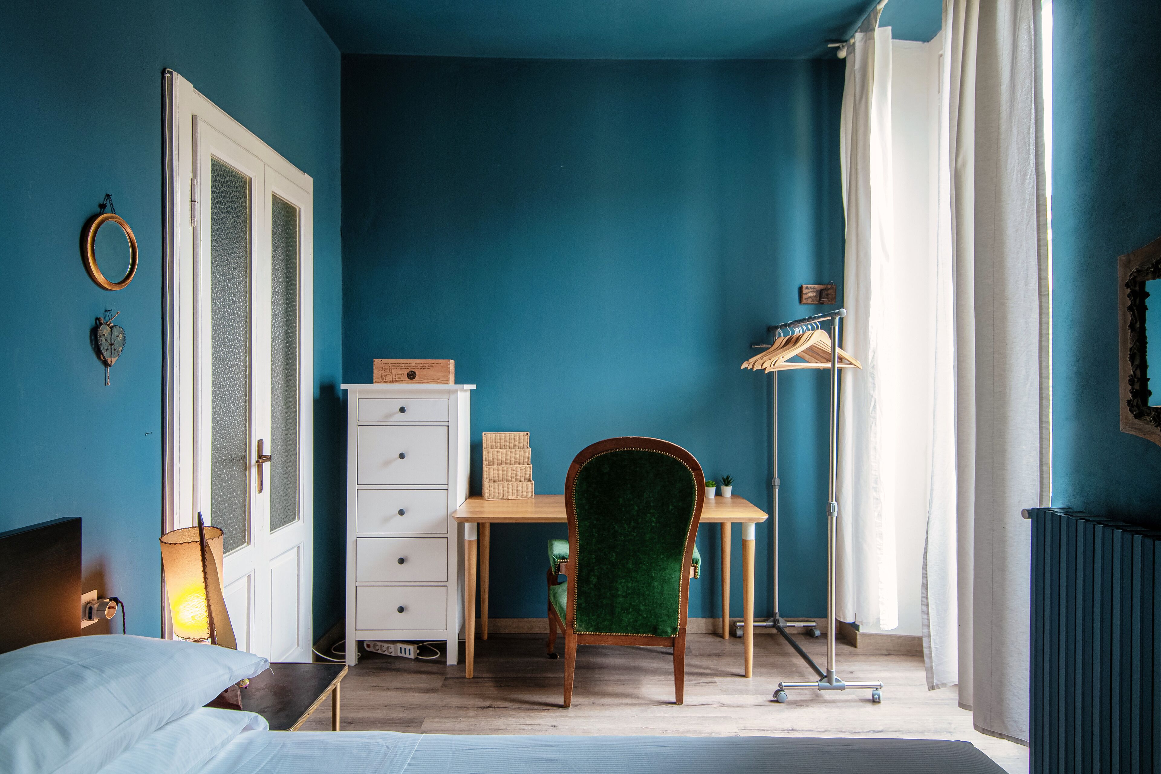 Una habitación con cama, escritorio, silla, cómoda y radiador.