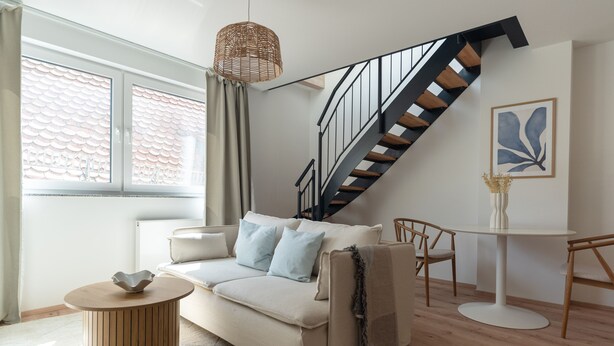 Een moderne woonkamer met een bank, een ronde salontafel, een eettafel en een trap.