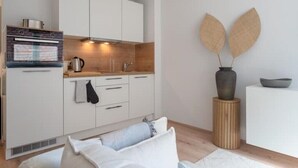 Een moderne keuken met witte kasten, een ingebouwde oven en een houten aanrecht. Er staat een vaas met twee decoratieve bladeren op een houten kruk naast de gootsteen.